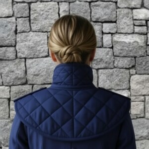 May include: A navy blue quilted jacket with a high collar and shoulder detailing. The jacket features a diamond pattern on the upper back and shoulders. The person's hair is styled in a bun.