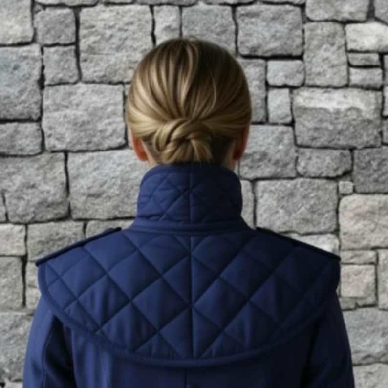 May include: A navy blue quilted jacket with a high collar and shoulder detailing. The jacket features a diamond pattern on the upper back and shoulders. The person's hair is styled in a bun.