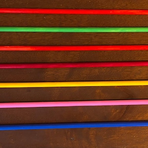 May include: Seven colorful wooden arrows with painted designs on the fletching. The arrows are red, green, red, burgundy, yellow, pink, and blue. The fletching features patterns in white, blue, and yellow.
