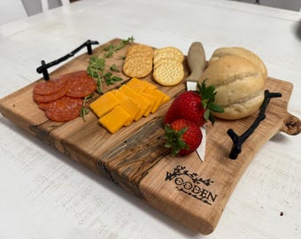 May include: A wooden serving board with black metal handles, holding an assortment of food items. Sliced pepperoni, cheddar cheese, crackers, strawberries, and bread rolls are arranged on the board. The board has the word "WOODEN" printed on it.