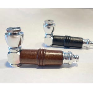 May include: Two metal pipes with wooden and black leather stems. The pipes have a silver finish on the bowl and mouthpiece. One pipe has a brown wooden stem, and the other has a black leather stem.