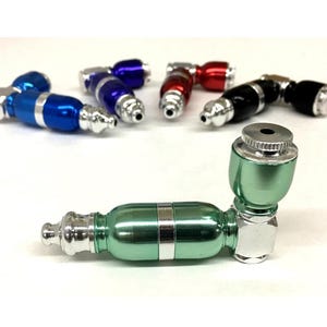 May include: A collection of colorful metal pipes in various shades, including blue, red, black, and green. The pipes have a curved design with silver accents and a bowl at one end. The main pipe is green with silver details.