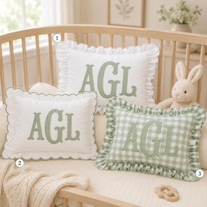 May include: Three rectangular decorative pillows featuring the embroidered sage green letters AGL. One white pillow has a ruffled edge, one white pillow has a scalloped edge, and one sage green and white gingham checkered pillow has a ruffled edge.