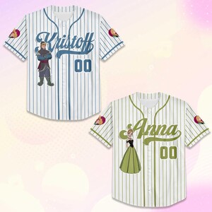 Puede incluir: Dos camisetas de b&eacute;isbol, una blanca con finas rayas azules y el nombre "Kristoff", la otra verde con finas rayas blancas y el nombre "Anna". Cada camiseta tiene un gr&aacute;fico de personaje y el n&uacute;mero "00".
