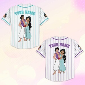 Puede incluir: Camiseta de b&eacute;isbol blanca con finas rayas azules verticales. La parte posterior presenta una imagen de dibujos animados de Aladdin y Jasmine, con el texto "YOUR NAME" encima de la imagen. Las mangas tienen una imagen de dibujos animados de Jasmine.