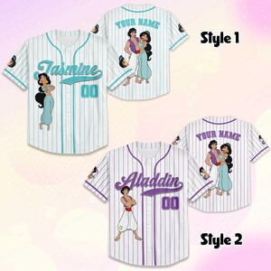 Puede incluir: Camisetas de b&eacute;isbol blancas con rayas finas, con personajes de dibujos animados y nombres. Una camiseta tiene "Jasmine" y "00" en verde azulado, la otra "Aladdin" y "00" en morado. Ambas tienen arte de personajes.