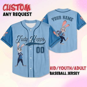 May include: Pale blue baseball jersey with the character Judy Hopps from Zootropolis. The jersey has "Judy Hopps" and the number "00" on the front. The back says "YOUR NAME". The sleeves are dark blue. The text "CUSTOM ANY REQUEST" is at the top.