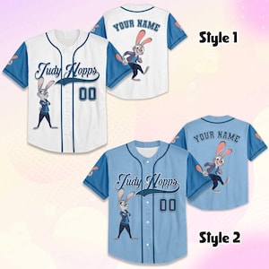 May include: Two baseball jerseys, one white and one light blue, featuring the character Judy Hopps. The white jersey has blue sleeves and trim, with "Judy Hopps" and the number "00" on the front. The light blue jersey has matching details.