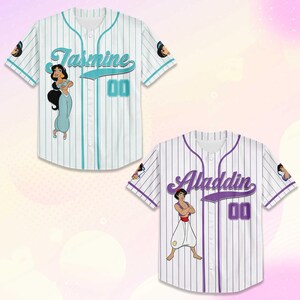 Puede incluir: Dos camisetas de b&eacute;isbol blancas. Una con rayas finas turquesas, el nombre "Jasmine" en turquesa y el n&uacute;mero "00". La otra con rayas finas moradas, el nombre "Aladdin" en morado y el n&uacute;mero "00". Ambas camisetas presentan gr&aacute;ficos de personajes.