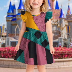 May include: A sleeveless dress featuring a patchwork pattern of yellow, pink with black swirls, teal, and dark pink sections separated by black stitched lines. The dress has ruffled cap sleeves and a round neckline, showcasing a colorful design.