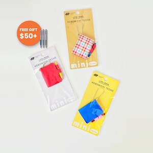 Può includere: Tre mini taccuini portachiavi Hobonichi Techo in confezioni singole. Uno presenta una copertina a quadri rossi, blu e bianchi, uno è rosso tinta unita e uno è blu tinta unita. Ognuno include una minuscola penna e una catenella argentata.