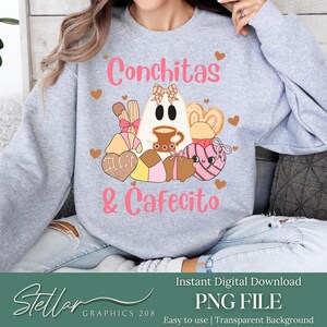 Könnte beinhalten: Ein hellgraues Sweatshirt mit den Worten "Conchitas & Cafecito" in Rosa. Das Design zeigt einen Geist, der eine Kaffeetasse hält, umgeben von Gebäck und Herzen. Das Bild enthält auch den Text "Instant Digital Download" und "PNG FILE".