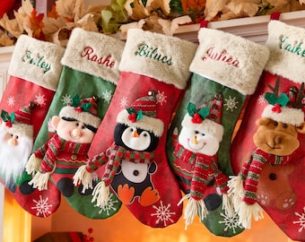 May include: Five Christmas stockings with personalized names embroidered on the top cuff. Each stocking features a different festive character: Santa, an elf, a penguin, a snowman, and a reindeer. The stockings are red and green.