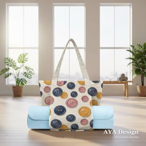 May include: A light blue yoga mat is held in place by a tote bag. The tote bag has a cream background with a pattern of colourful buttons in shades of pink, yellow, and navy blue. The bag has cream-coloured handles.