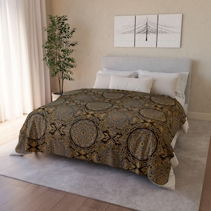 May include: A bed with a decorative blanket featuring a repeating circular pattern in gold, blue, and black. The bed has white pillows and a light grey headboard. A potted tree is next to the bed.