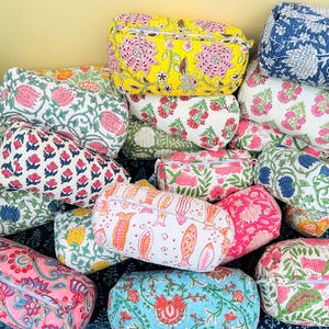 Op de afbeelding: Een verzameling kleurrijke, gewatteerde cosmetische tassen met bloempatronen. De tassen hebben verschillende ontwerpen, waaronder roze, blauwe, gele en groene bloemenprints. Elke tas heeft een ritssluiting.