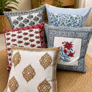 May include: A collection of five square throw pillows featuring various block-printed designs. Patterns include black leaf motifs, blue and green floral prints, red floral patterns, a central red flower, and mustard yellow ornate medallions.
