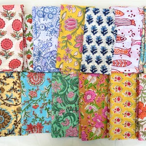 May include: A selection of folded fabric napkins featuring diverse floral and patterned designs. The colours include pink, red, blue, yellow, and green. The napkins are arranged in rows, displaying the variety of prints.