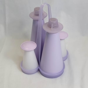 May include: A vintage lavender and white plastic condiment set. The set includes two tall, cone-shaped bottles, two smaller bottles, and a handle for easy carrying. The lids are a lighter shade of lavender.