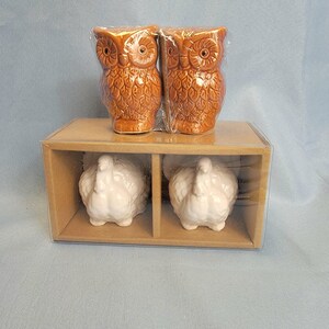 May include: A set of ceramic owl and turkey figurines. Two brown owl figurines are on top, and two white turkey figurines are below, all in a brown box with clear plastic wrapping. The owls have detailed feather patterns.