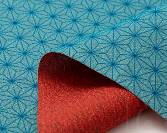 Può includere: Un tessuto turchese con un motivo geometrico a stelle. Il tessuto è piegato per rivelare un lato inferiore rosso.