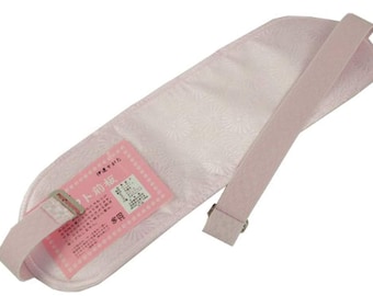 May include: A light pink obi-ita, a traditional Japanese garment accessory. The rectangular pad features a floral pattern and a matching strap with a metal buckle. A pink label with Japanese text is attached.