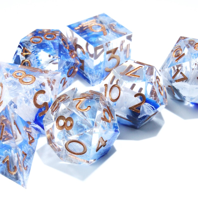 May include: Set of seven polyhedral dice with a blue and white marbled design. The dice have gold-colored numbers and are made of clear resin. The dice are for tabletop games.