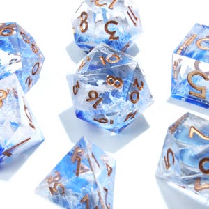 May include: A collection of polyhedral dice with a blue and white marbled design. The dice have gold-colored numbers and are made of a clear resin material. The dice are for tabletop games.