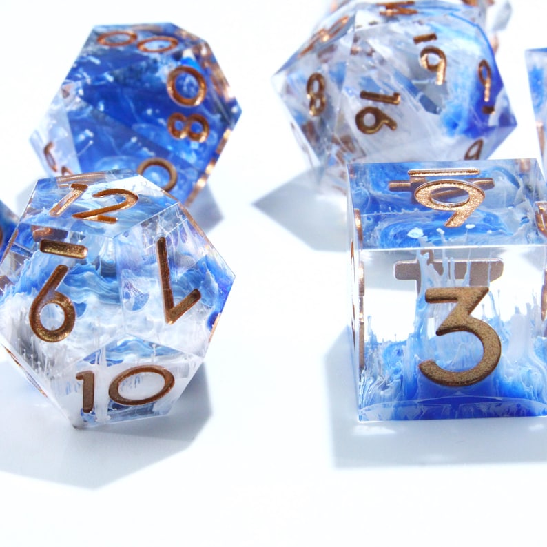May include: Close-up of several polyhedral dice. The dice are clear with blue and white swirls, and gold-colored numbers. The dice are in various shapes, including a cube and a 20-sided die. The dice are on a white surface.