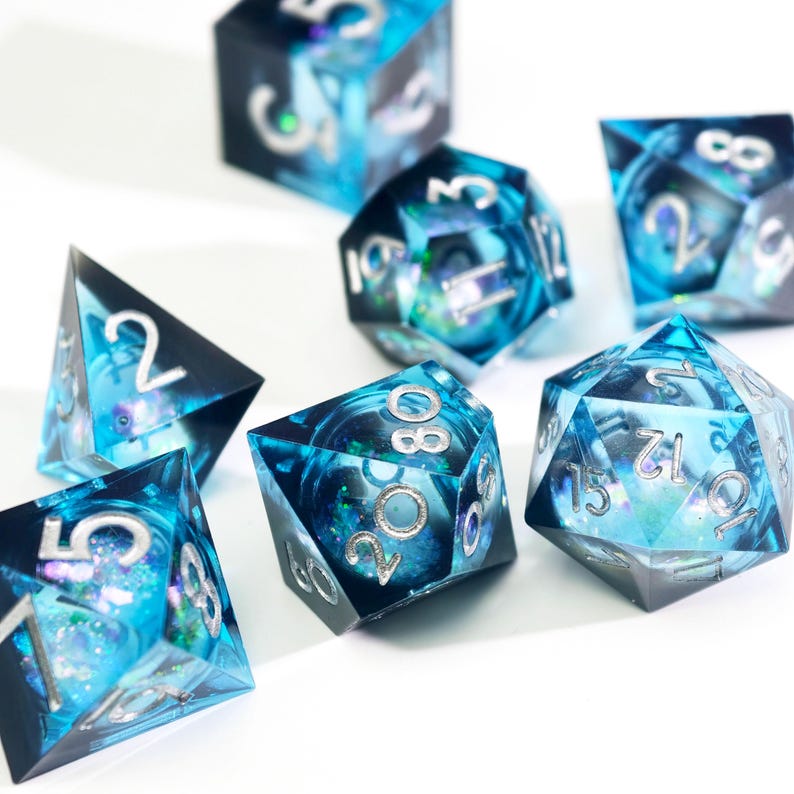May include: A set of seven polyhedral dice with a celestial theme. The dice are a translucent blue with swirling patterns and silver numbering. The dice are designed for tabletop role-playing games.