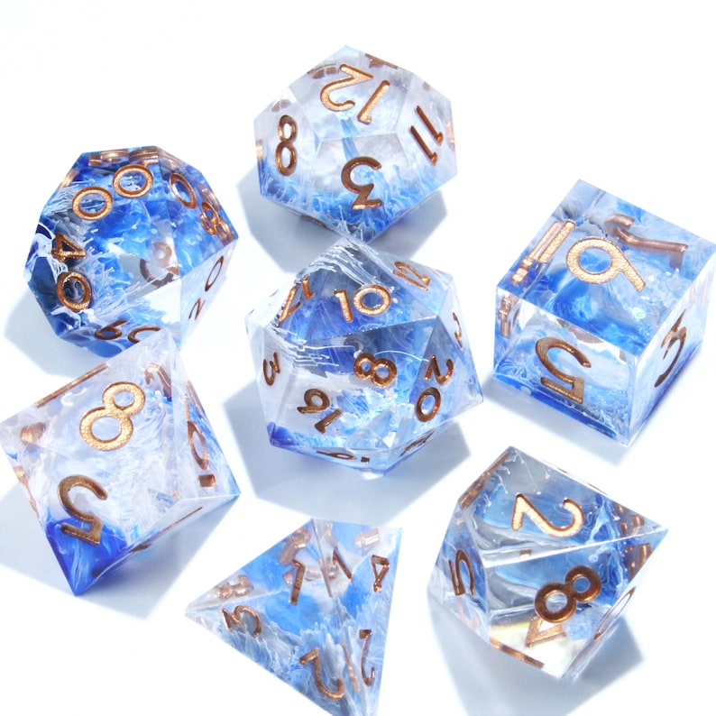 May include: Set of seven polyhedral dice with a clear resin base, blue and white internal swirls, and gold-colored numbers. The dice are in various geometric shapes, including a d4, d6, d8, d10, d12, and d20, perfect for tabletop gaming.