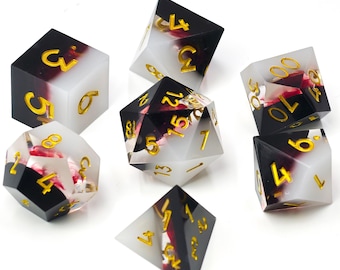 May include: A set of seven polyhedral dice made of translucent white and opaque black resin with gold-coloured numbers. The dice contain embedded red floral elements visible through the clear sections, including a d20, d12, d10, d8, d6, d4, and percentile die.