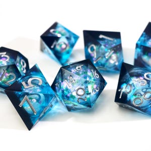 May include: A set of polyhedral dice with a blue and black design. The dice have silver numbering and a shimmering, galaxy-like interior. The dice are made of a clear resin material and are designed for tabletop gaming.