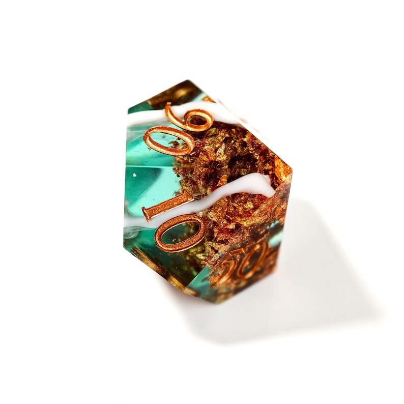 Op de afbeelding: Een polyhedrale dobbelsteen met een turquoise en gouden binnenkant, met koperkleurige cijfers. De dobbelsteen heeft een wit, wervelend ontwerp en staat tegen een witte achtergrond. De cijfers zijn duidelijk zichtbaar.