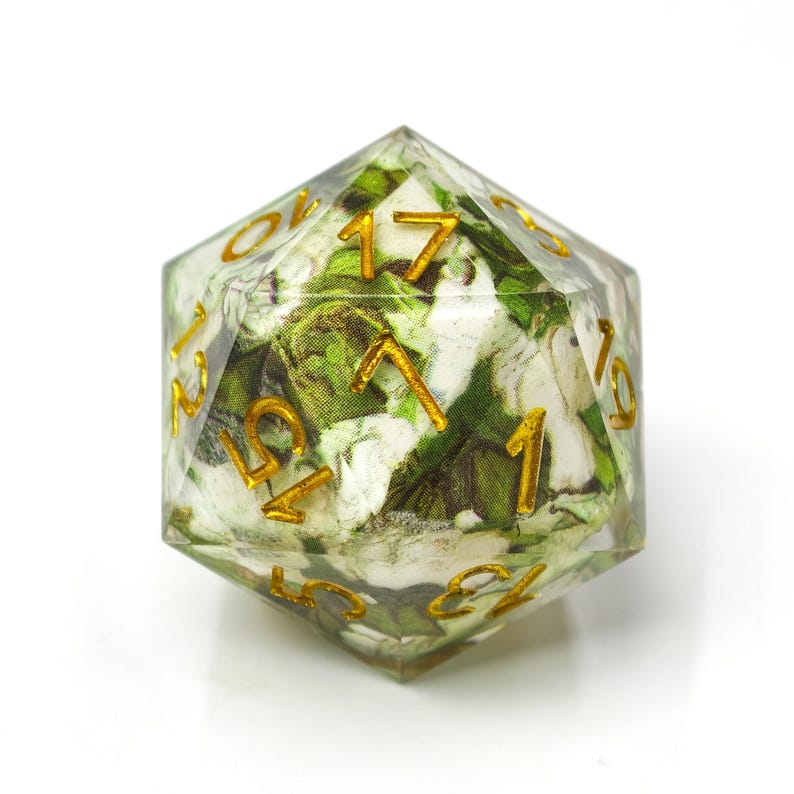K&ouml;nnte beinhalten: Ein zwanzigseitiger W&uuml;rfel aus klarem Harz mit einem eingebetteten wei&szlig;en und gr&uuml;nen Blumenstoffmuster. Die Zahlen auf den Seiten des W&uuml;rfels sind eingraviert und mit goldener Metallic-Farbe ausgef&uuml;llt, was einen Kontrast zum Blumenmuster bildet.