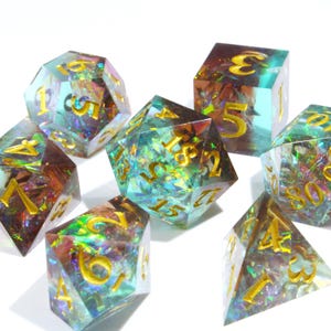 Puede incluir: Un conjunto de siete dados poliédricos iridiscentes con numeración dorada. Los dados son una mezcla de verde azulado, morado y dorado, con un efecto brillante y brillante. Estos dados están diseñados para juegos de rol de mesa.