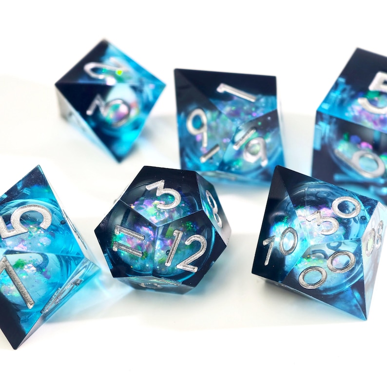 May include: A set of seven polyhedral dice with a celestial theme. The dice are a translucent blue with silver numbering and internal iridescent inclusions. The dice are designed for tabletop role-playing games.