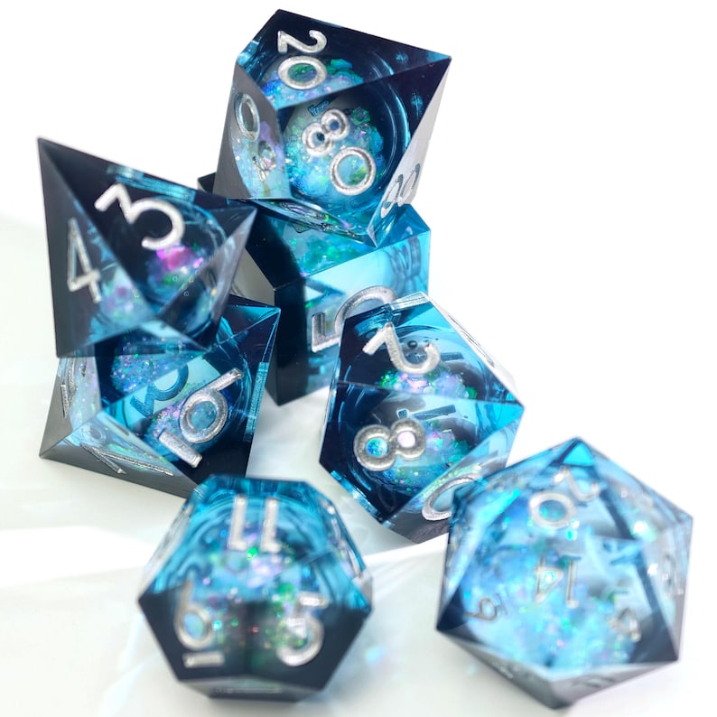 May include: A set of seven polyhedral dice with a blue and teal translucent design. The dice have silver numbering and internal glitter and decorative elements. The dice are for tabletop games.