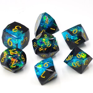 May include: A set of seven polyhedral dice made of dark resin with embedded iridescent blue and green foil flakes. Each die features sharp edges and engraved numbers filled with gold paint, including a d20, d12, d10, d8, d6, d4, and a percentile die.