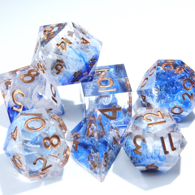 May include: A set of seven polyhedral dice for tabletop games. The dice are clear with blue and white swirls, and gold-colored numbers. The dice include a D4, D6, D8, D10, D12, D20, and a percentile die.