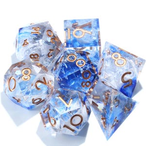 May include: A set of seven polyhedral dice with a blue and white marbled design. The dice have gold-colored numbers and edges. The set includes a D4, D6, D8, D10, D12, D20, and a percentile die, perfect for tabletop gaming.