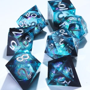 Puede incluir: Un conjunto de siete dados poliédricos de diferentes formas. Los dados son de resina azul verdoso translúcida con numeración plateada y purpurina interna. Diseñados para juegos de rol de mesa.