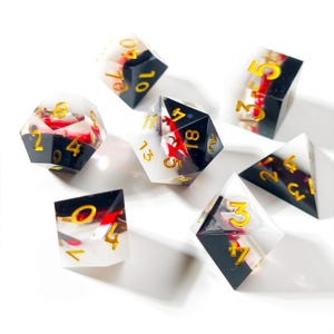 May include: Set of seven polyhedral dice with a black and white color scheme, gold numbering, and red accents. The dice are made of a clear resin material, with a variety of shapes including a d4, d6, d8, d10, d12, and d20.