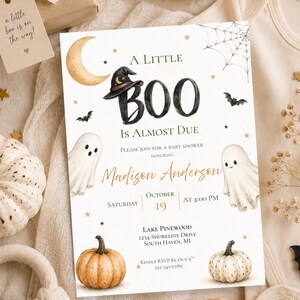 May include: A rectangular baby shower invitation card featuring a watercolor design with a crescent moon, a witch hat, two ghosts, pumpkins, bats, and a spider web. The text reads A LITTLE BOO IS ALMOST DUE, honoring Madison Anderson, Saturday October 19 at 4:00 PM, Lake Pinewood, 1234 Shoreline Drive, South Haven, MI, and RSVP by Oct 9th 222-345-6789.