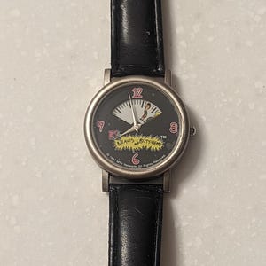 May include: A vintage wristwatch with a black leather band and a silver-toned case. The watch face is black with white and yellow accents, featuring the numbers 12, 3, 6, and 9. The watch band is approximately 9 inches long.