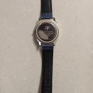 May include: A silver watch with a blue leather strap. The watch face is not visible, but the back is engraved with "ANDRE FRANCOIS STAINLESS STEEL BACK HIGH QUALITY JAPAN MOVT". The strap is black on the underside.
