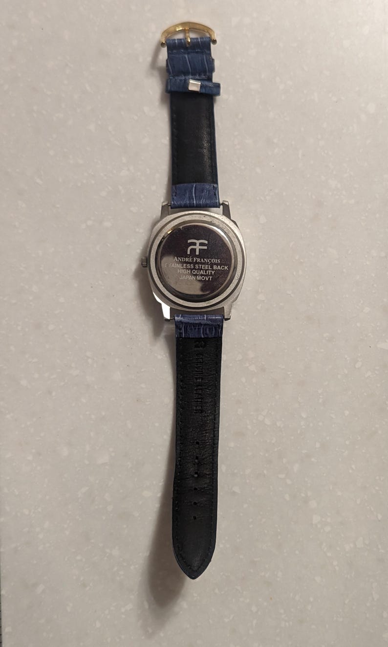 May include: A silver watch with a blue leather strap. The watch face is not visible, but the back is engraved with "ANDRE FRANCOIS STAINLESS STEEL BACK HIGH QUALITY JAPAN MOVT". The strap is black on the underside.