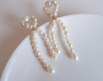 May include: A pair of pearl earrings. Each earring has a loop of small pearls at the top, connected to a cascade of varying-sized pearls that dangle downwards. The pearls are creamy white and have a subtle lustre, with a small gold accent.