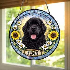 May include: Round stained glass window featuring a black Newfoundland dog with its tongue out, surrounded by sunflowers and daisies. The dog's name, "FINN", is on a banner at the bottom. The window is framed with a black metal chain.