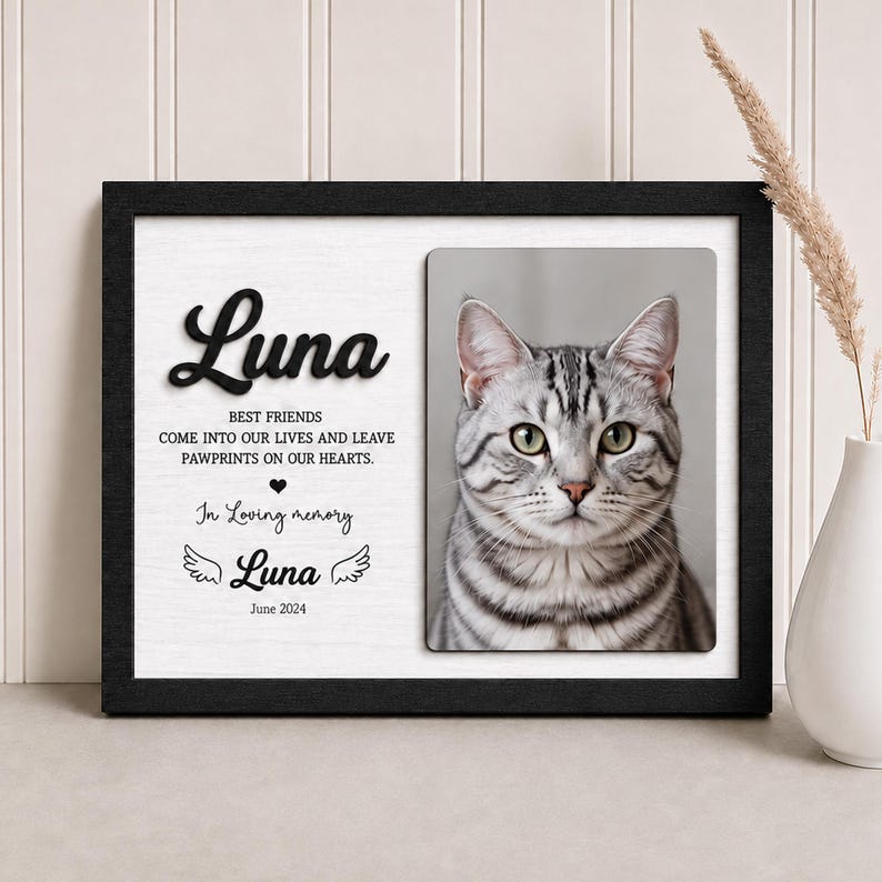 Puede incluir: Un marco de pared conmemorativo negro que presenta el retrato de un gato atigrado plateado. El texto dice: Luna, BEST FRIENDS COME INTO OUR LIVES AND LEAVE PAWPRINTS ON OUR HEARTS, In Loving memory, Luna, June 2024, con dos peque&ntilde;as alas de &aacute;ngel.